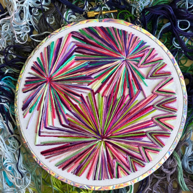 an abstract, multicolour cross stitch with pink, purple, yellow and blue tones.