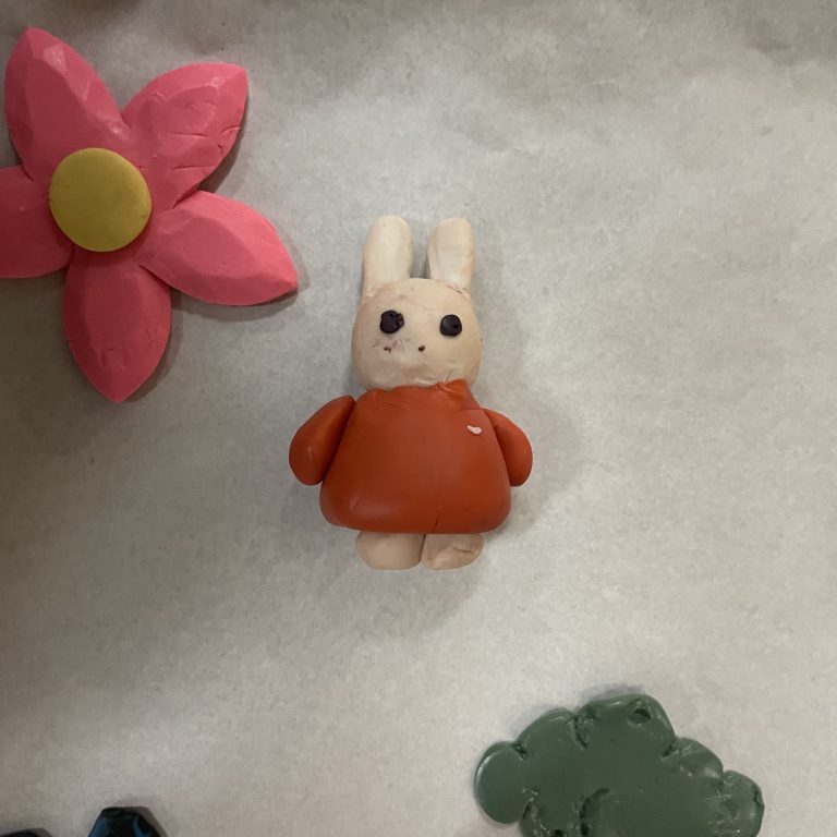 A polymer clay figure resembling character Miffy. Miffy is sitting on a baking sheet.